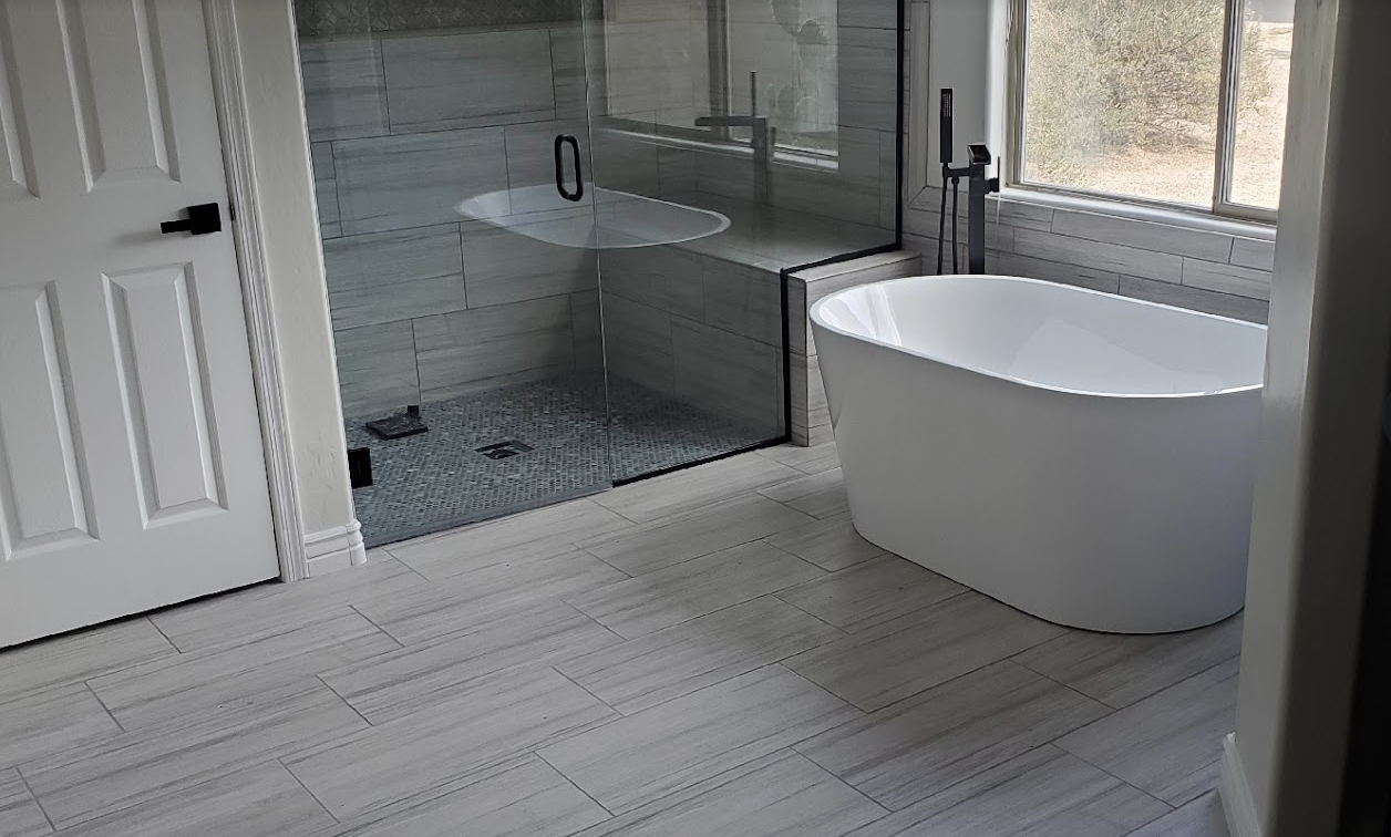 Freestanding tub with large-format gray tile flooring and walk-in shower